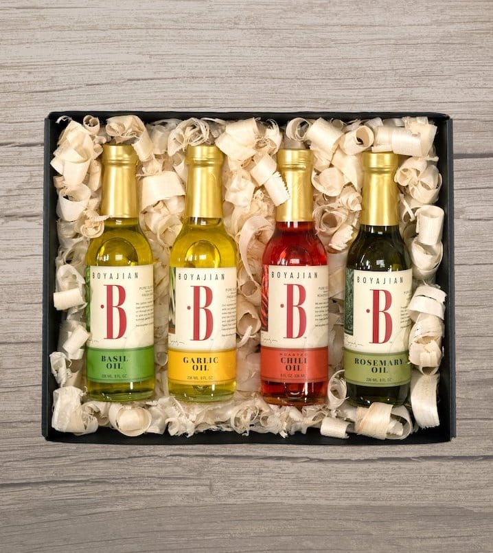 Four bottles of Boyajian flavored oils (Basil, Garlic, Chili, Rosemary) in a black gift box with shredded filler.