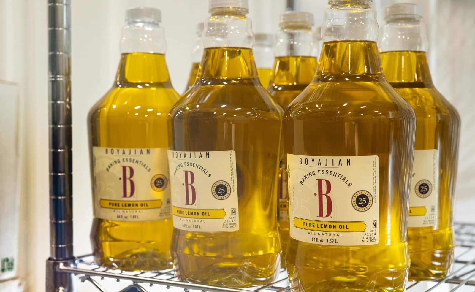 Multiple large clear plastic bottles of Boyajian Pure Lemon Oil on a metal shelf.